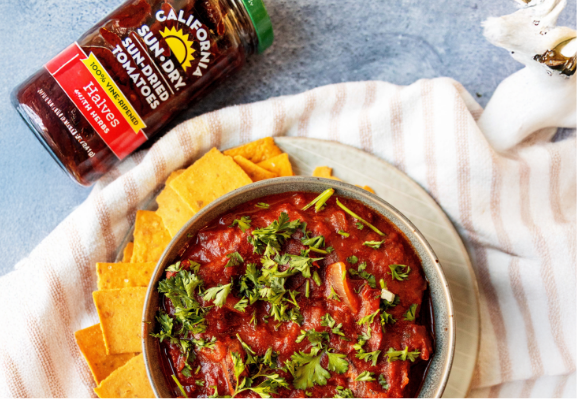 Overhead shot of a sun-dried tomato soup with cheese crackers on the side and a jar of California Sun Dry sun-dried tomato halves